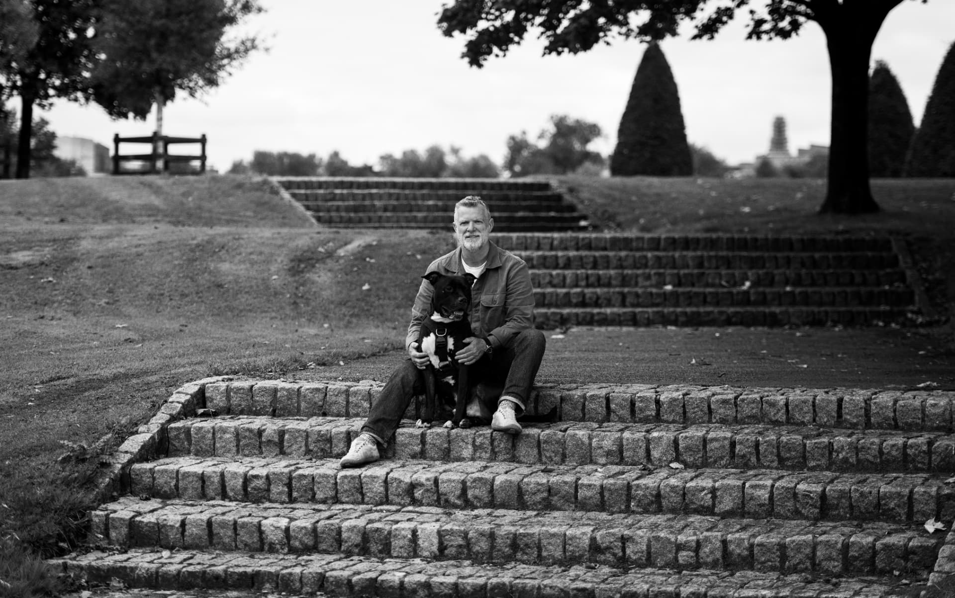 Black and white photograph of a dog resting beside its trainer in a Glasgow park