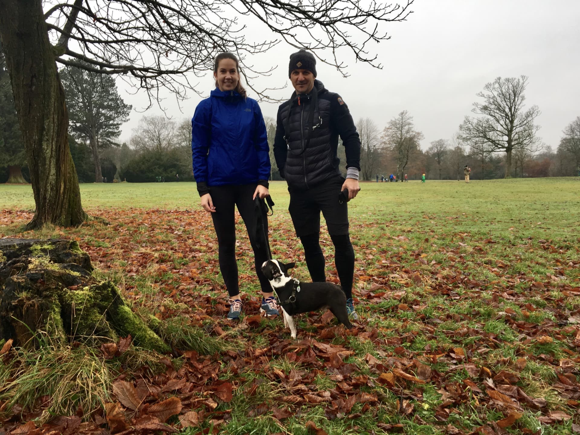 Couple walking their small black and white dog through a leaf-covered Glasgow park