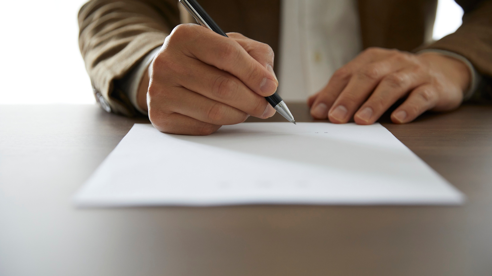 Person writing on a document at a desk while preparing an expert witness behavioural report
