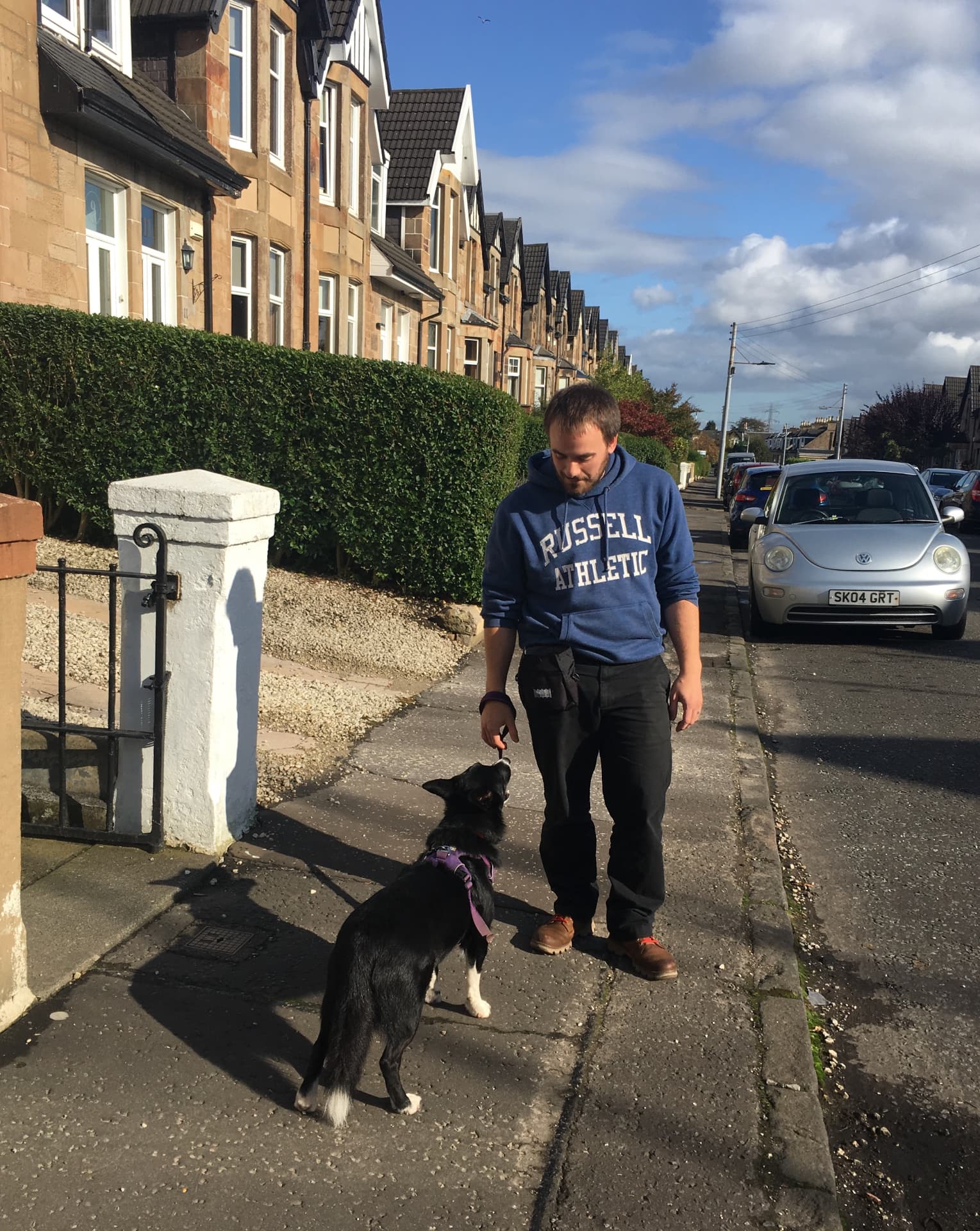Owner walking a collie type dog on the pavement of a residential Glasgow street