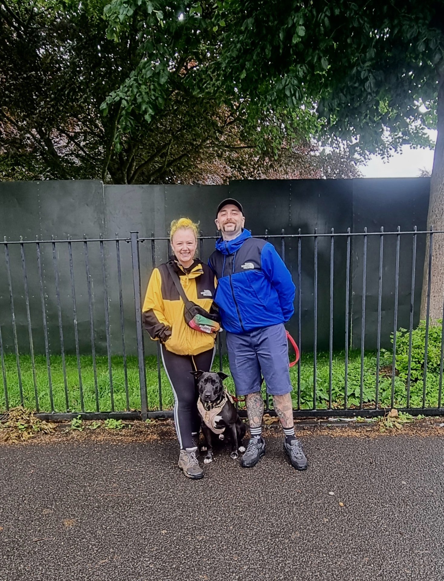 Couple with their black dog beside a metal fence on a Glasgow park walk